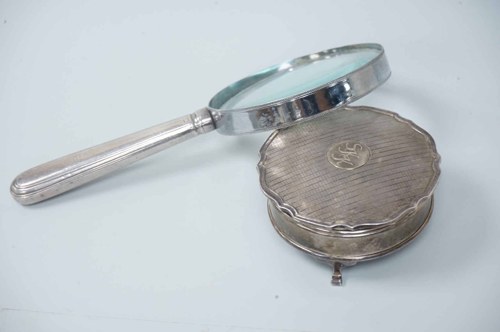 A George V silver mounted trinket box, by Adie Brothers, Birmingham, 1924, diameter 89mm. and a chrome magnifying glass, later added to a knife handle, handle by Goldsmiths & Silversmiths Co Ltd, London, 1894, 21.7cm.